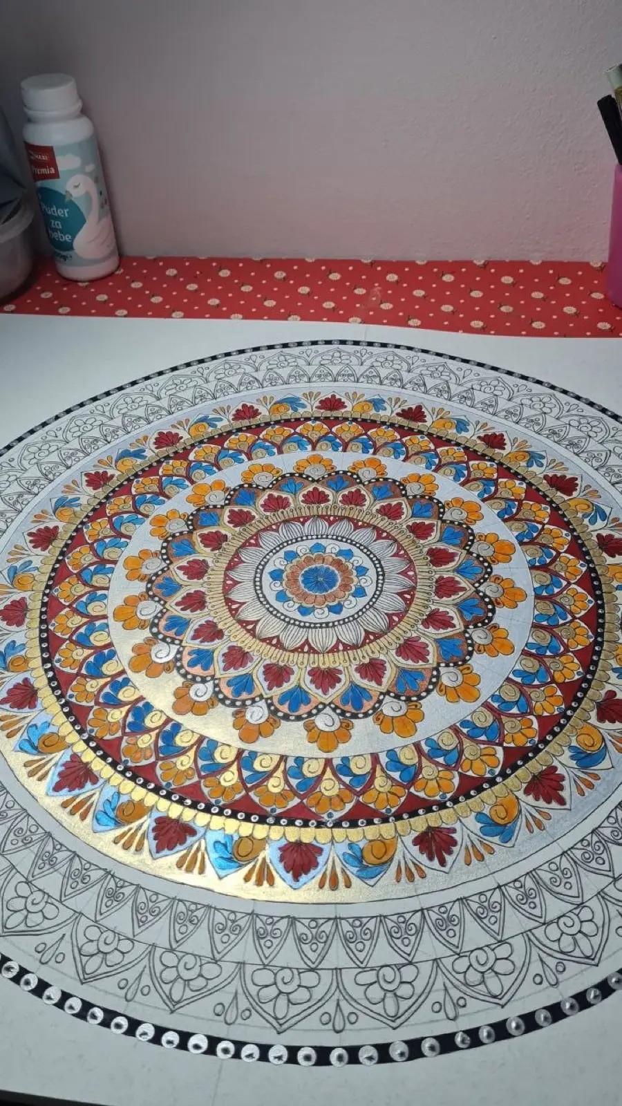 Mandala u toploj plavoj i zlatu, napola oslikana na stolu ateljea, sa geometrijom olovkom vidljivom na ivicama